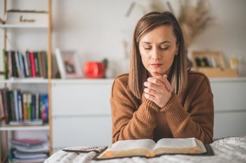 Woman prays while reading the bible on her faith journey