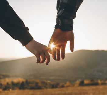 Couple lightly holding hands in field at sunset