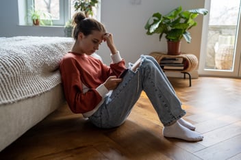 Young women looks sad, lonely, and depressed as she scrolls on her phone